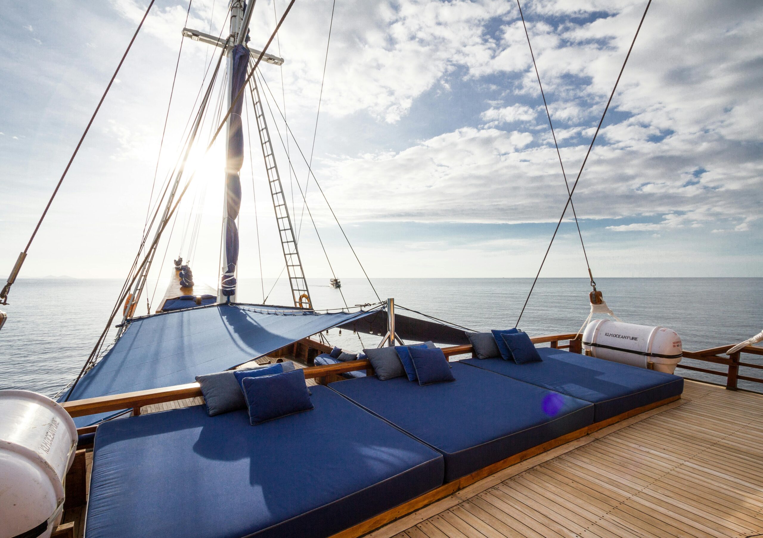Luxurious sailboat deck on a sunny day, featuring plush blue cushions and a serene ocean backdrop.