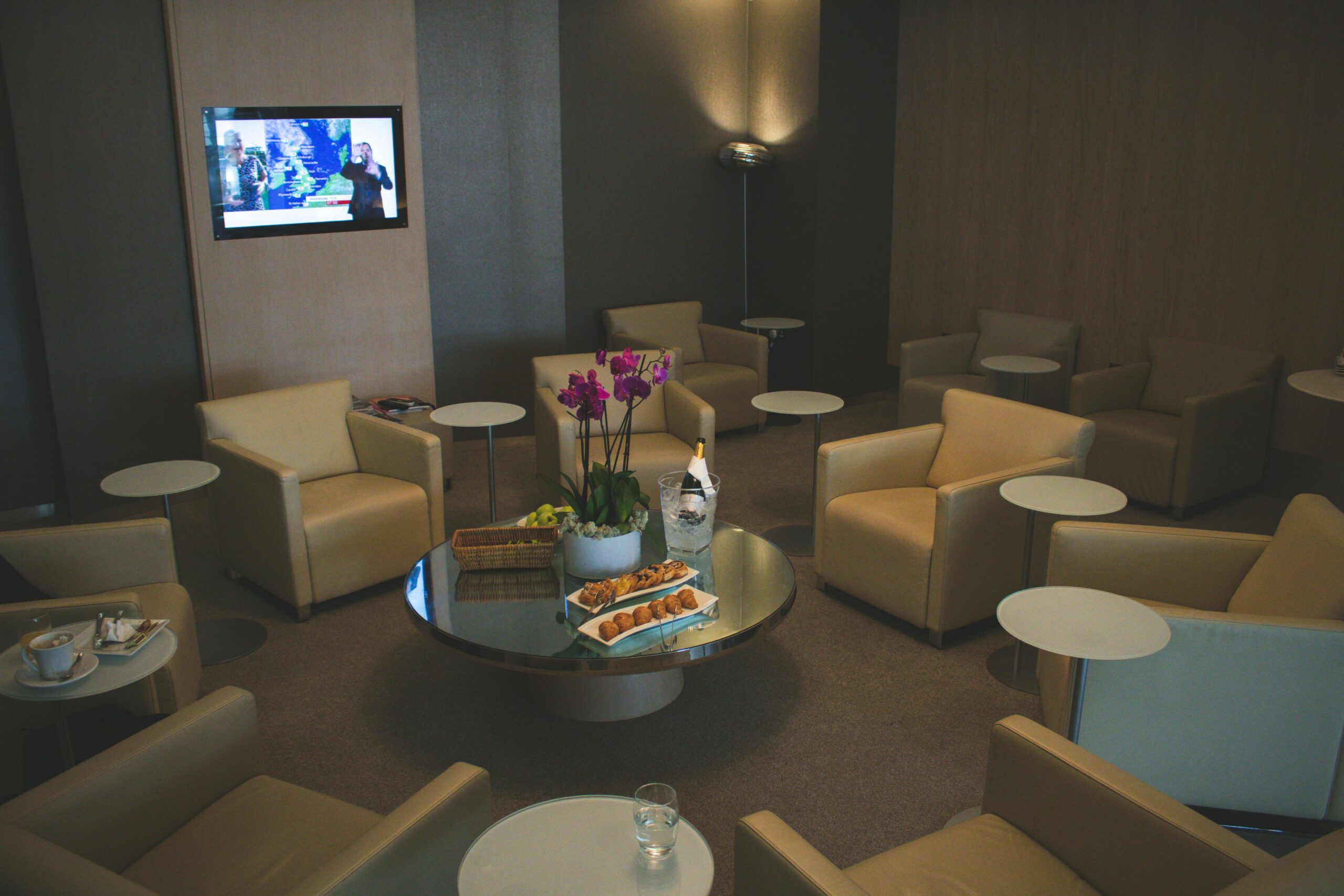 Elegant airport lounge with beige leather seats and orchid decor, offering comfort and luxury food service.