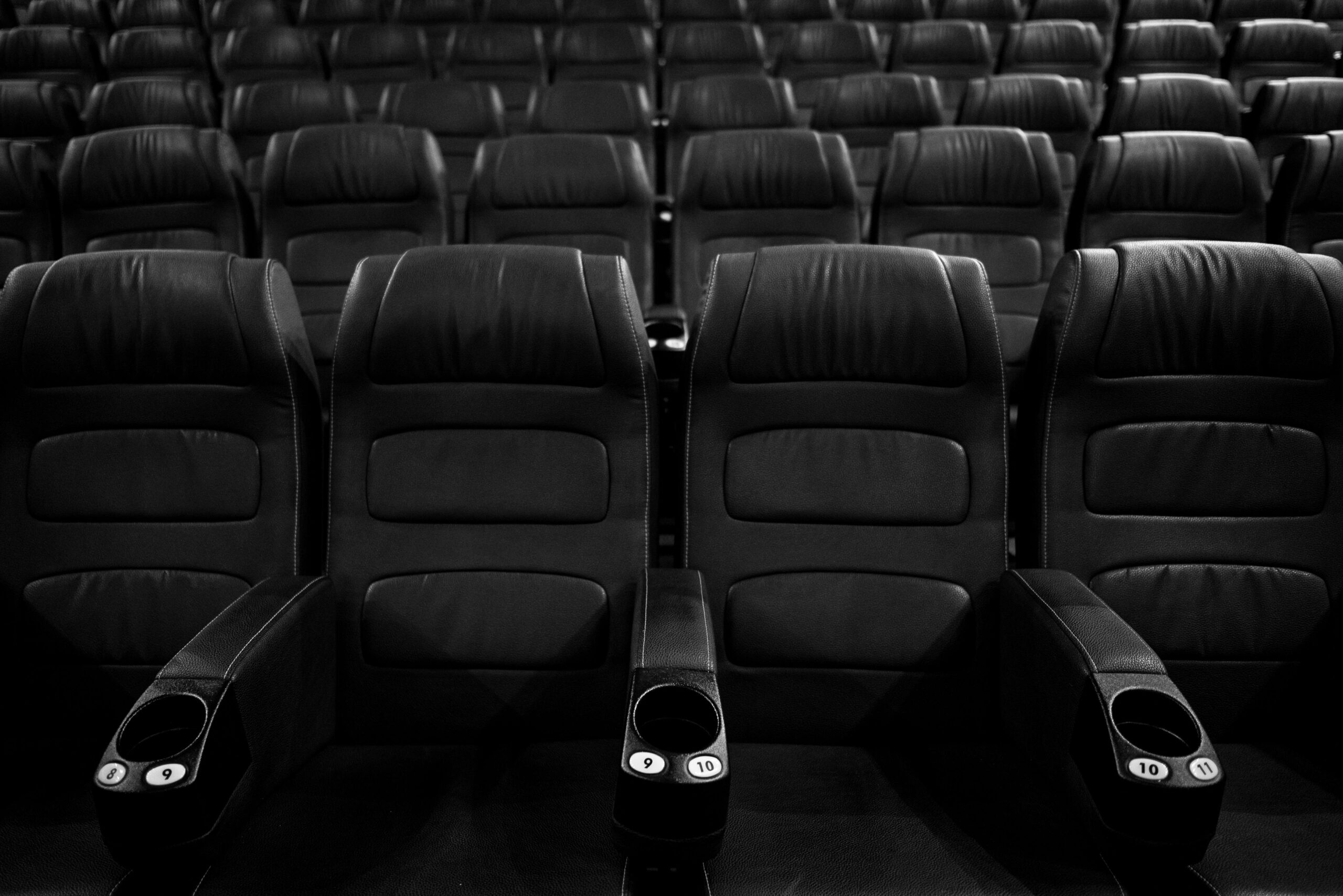 Grayscale image of empty leather cinema seats in a neat row.