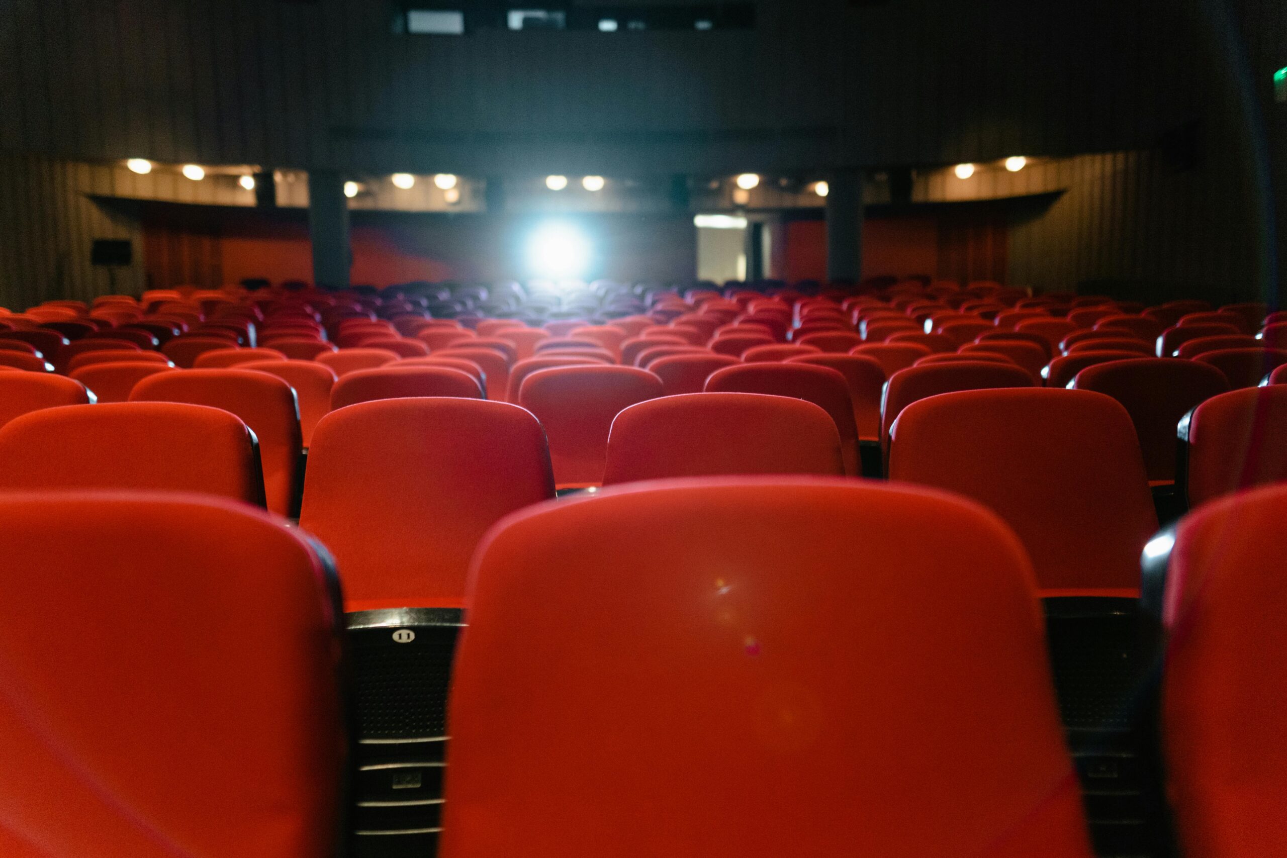A view of an empty cinema with rows of red seats facing the illuminated screen.