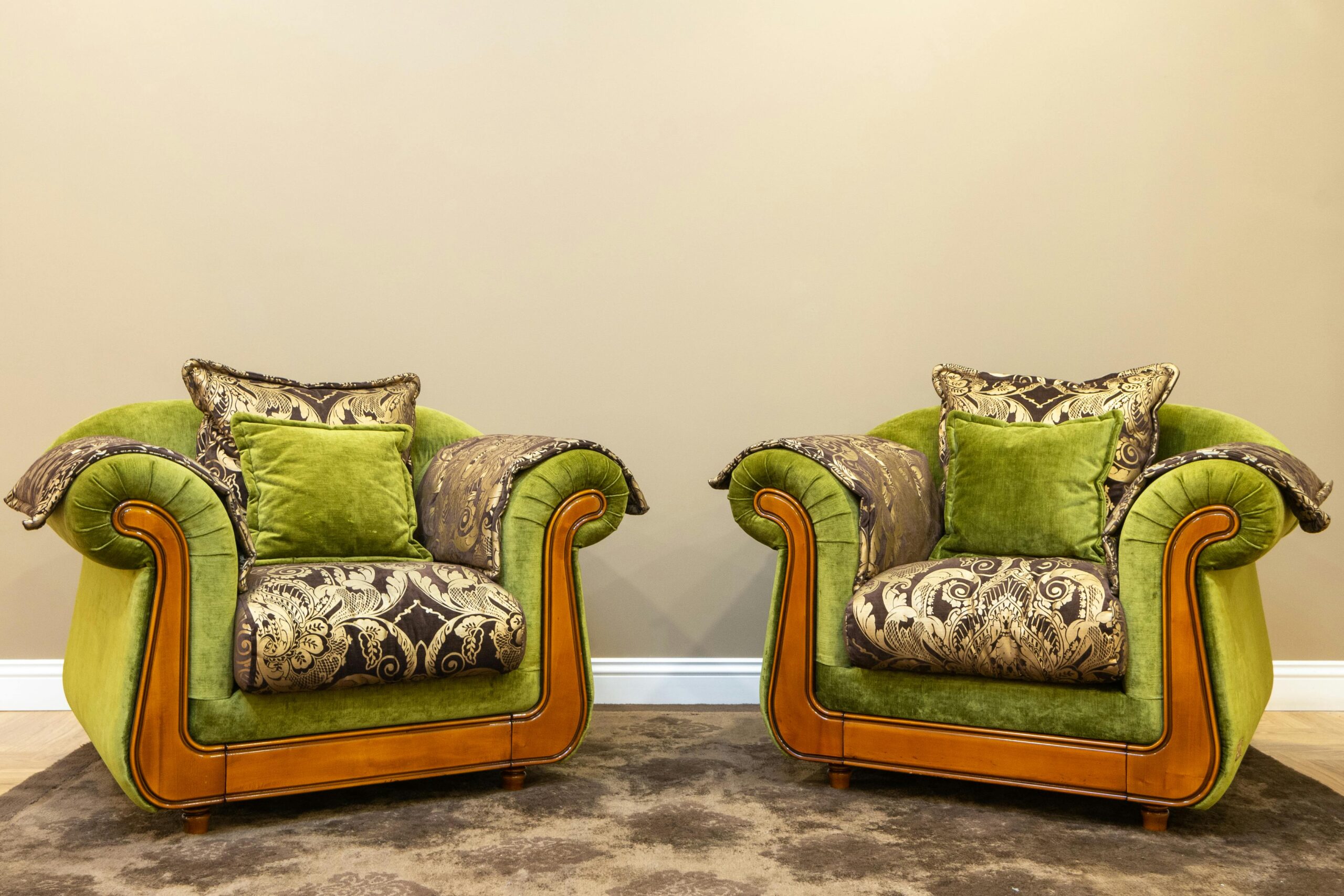 Two vintage green armchairs with ornate cushions set against a beige wall.